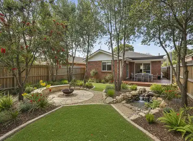 landscaping perth: two workers kneeling to lay paving slabs beside raised timber garden beds and a mini digger